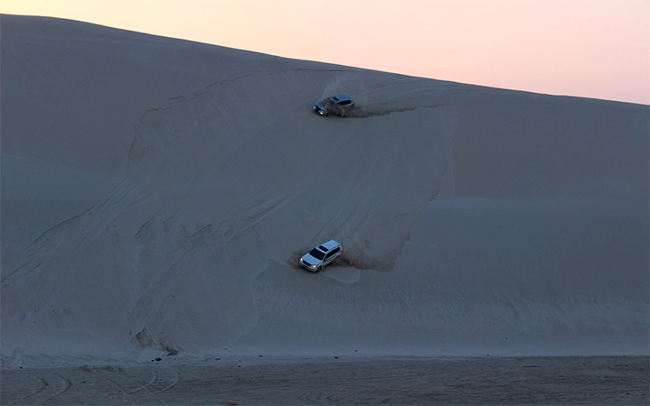 SUVs climbing dunes at night desert safari Qatar